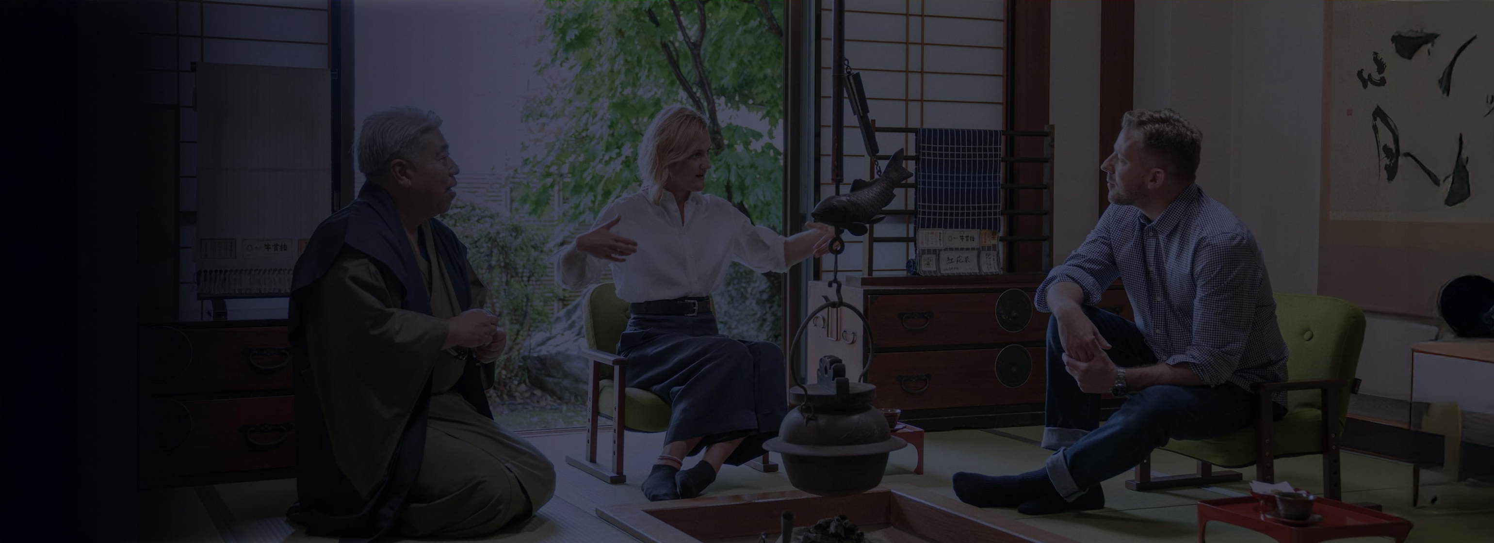 工房の中の写真。後ろには牛首紬の反物がたくさん並んだ棚がある。棚の名前では白人の男性と女性が反物を手に取って眺めている。