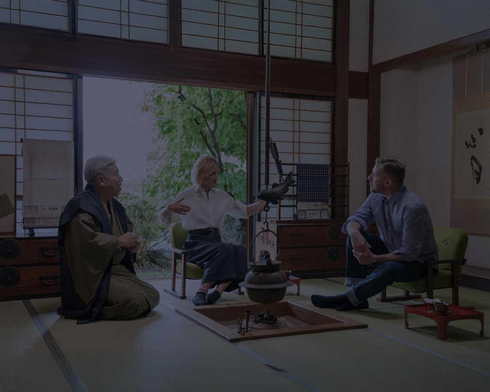 工房の中の写真。後ろには牛首紬の反物がたくさん並んだ棚がある。棚の名前では白人の男性と女性が反物を手に取って眺めている。