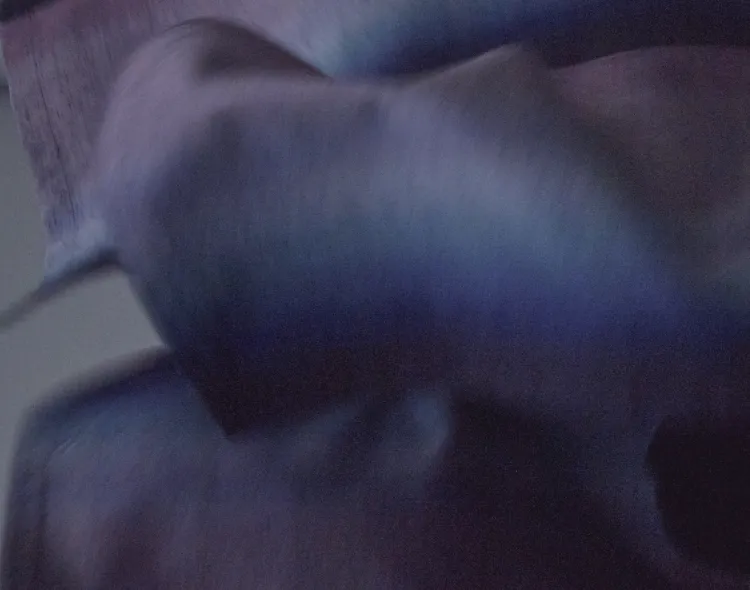 暗い照明の中で、深い紫と青のグラデーションが美しい米沢織のシャーリングコートの布が柔らかく波打っている様子。