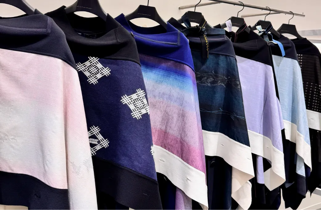 着物生地を使ったケープがハンガーに並び色や柄の違いが一望できる写真。藍色やグラデーションなど多様なデザイン展開が強調されている。