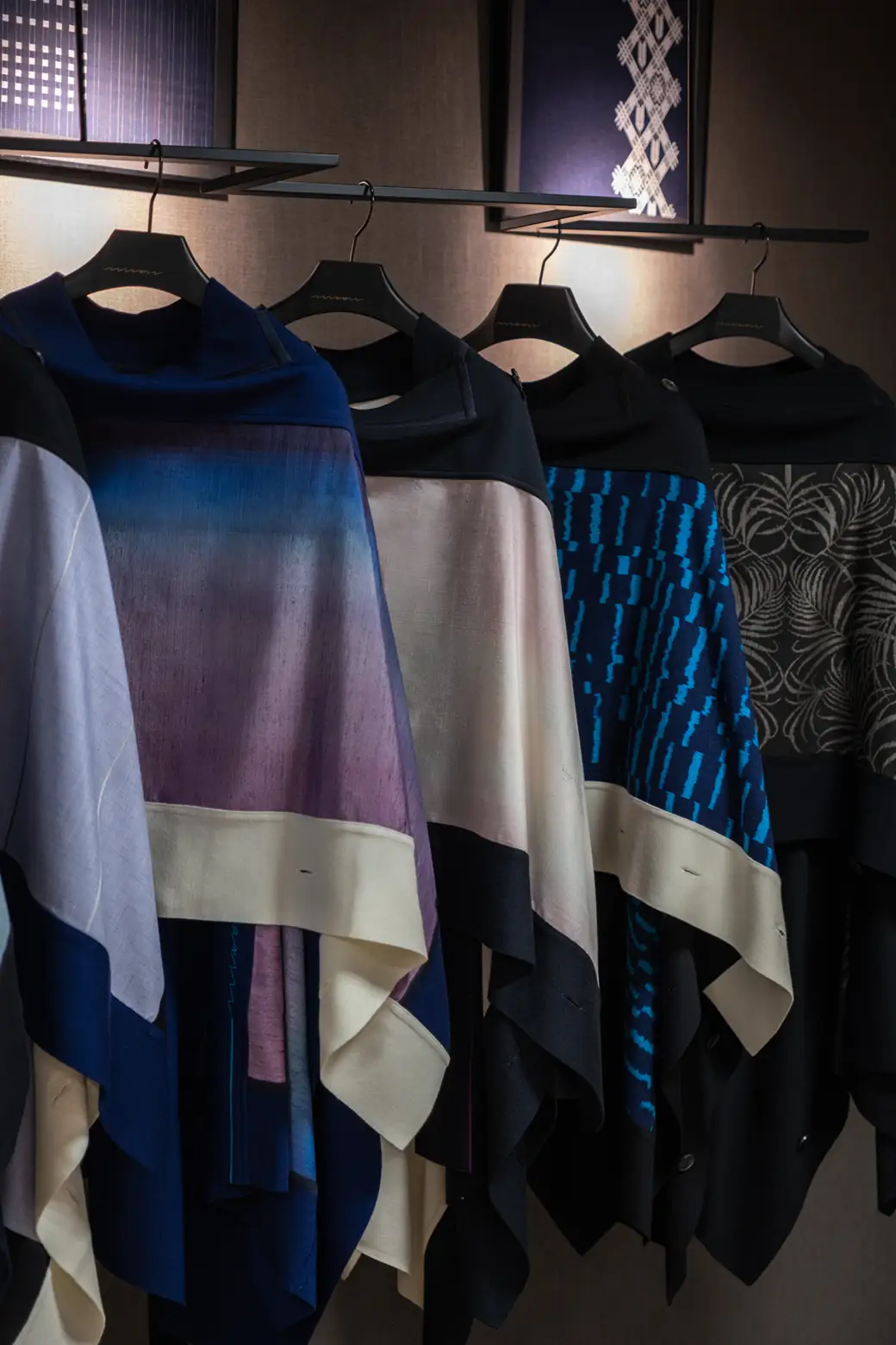 着物生地を使ったケープがハンガーに並び色や柄の違いが一望できる写真。藍色やグラデーションなど多様なデザイン展開が強調されている。